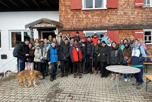 31 Personen, 28 Jugendliche und drei LehrerInnen, haben sich vor dem Schöntalhof zum Gruppenfoto aufgestellt. Alle lachen. Von Links trottet ein zotteliger alter Hund ins Bild.